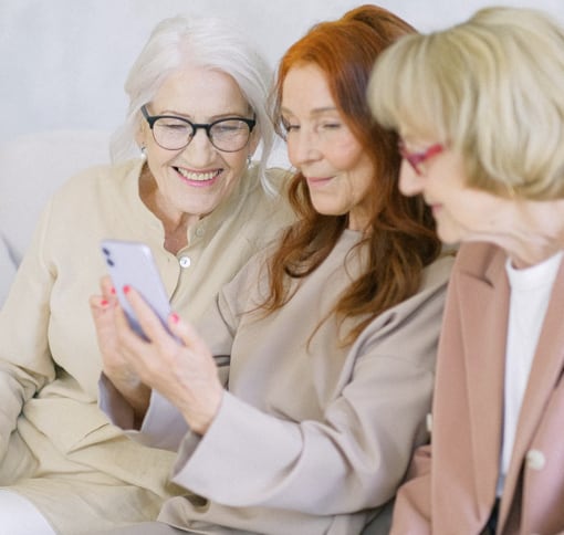 Three women seated closely together, engaged in a video call on a mobile phone.